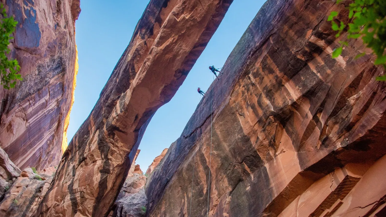Canyoneers rappelling beneath large natural sandstone bridge near Morning Glory Arch in Moab