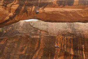 Canyoneering rappel beneath natural sandstone bridge near Morning Glory Arch in Moab Utah