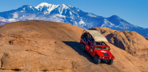 Hummer descending slickrock dune with La Sal Mountains behind
