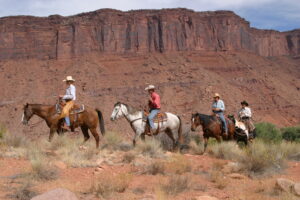Trail riders lined up on horseback with red rock formations behind