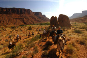 Horseback riders following trail at sunset among desert boulders
